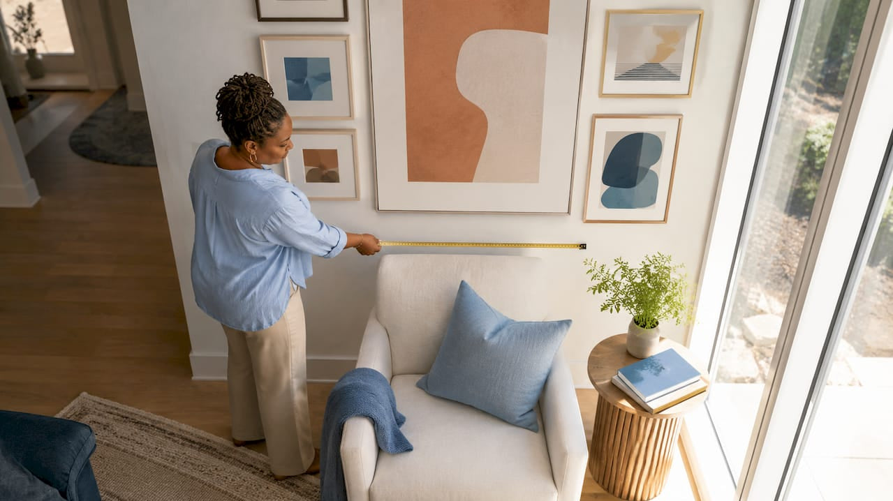 Woman measuring wall art over sofa in living room