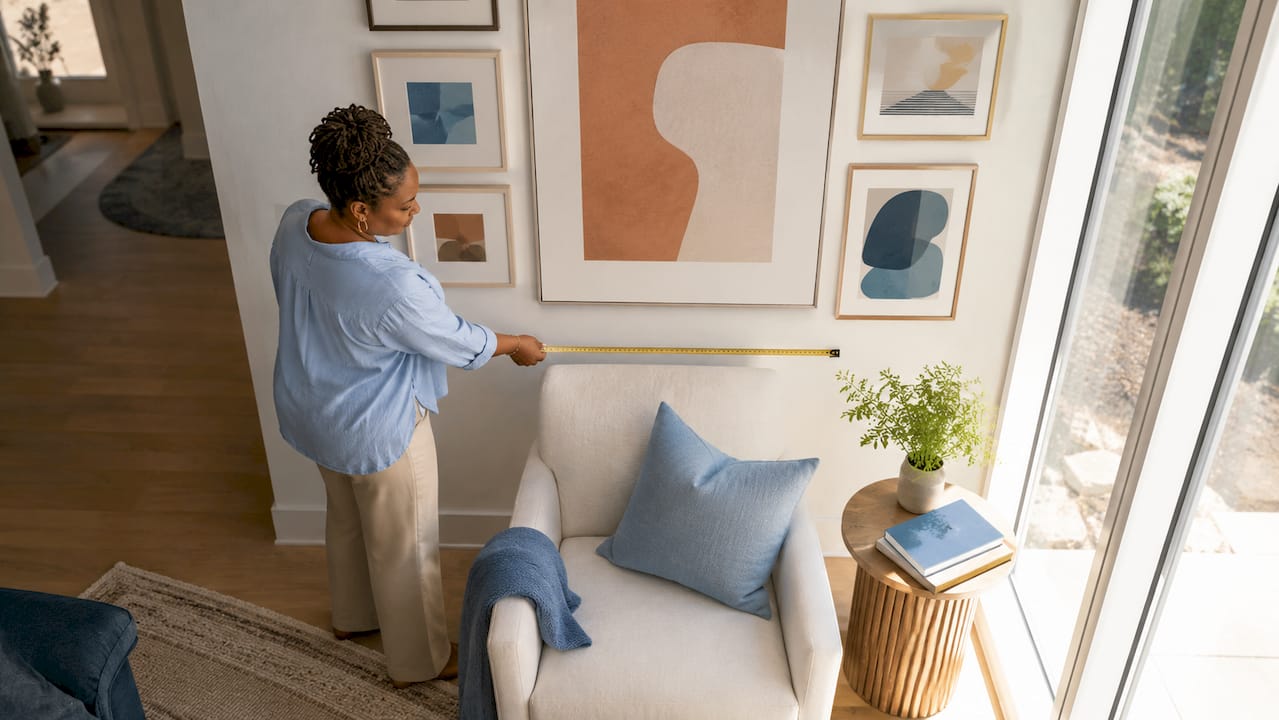 Woman measuring wall art over sofa in living room
